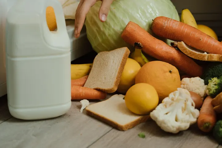 Человек собирает с пола кухни продукты, выпавшие из открытого холодильника